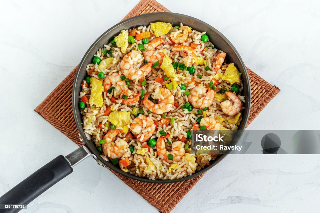 Shrimp Fried Rice in a Skillet Directly Above Horizontal Photo Shrimp Fried Rice in a Skillet on a Place Mat Top Down Flat Lay Photo on White Background Rice - Food Staple Stock Photo