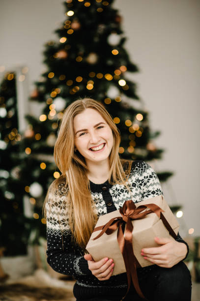 la chica abre un regalo. feliz navidad y felices fiestas. retrato de la joven con caja de regalos cerca del árbol de navidad. feliz nuevo año 2021 concepto. - fashionable party design home decorating fotografías e imágenes de stock