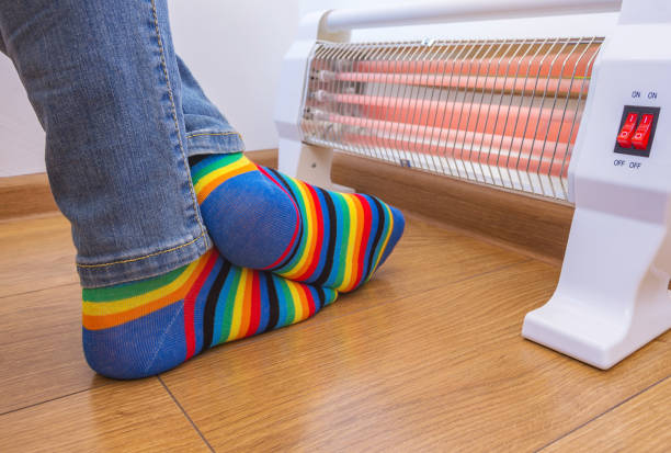 A person wearing bright rainbow-colored socks warms their frozen feet near a home electric heater. Infrared halogen heater at home. A person wearing bright rainbow-colored socks warms their frozen feet near a home electric heater. Infrared halogen heater at home. warms stock pictures, royalty-free photos & images