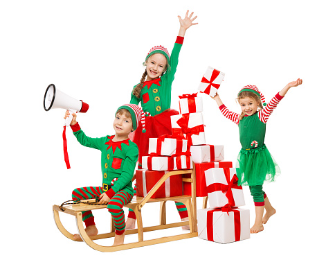 Funny Christmas Kids with Megaphone preparing a lot of New Year Gifts. Santa Claus Helpers, Cute Little Elves on Sleigh packing Christmas Present Boxes in Stack. Isolated White