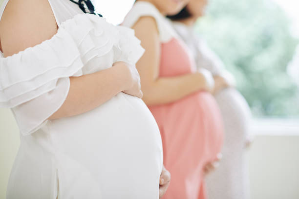 Group of pregnant young women standing in row and touching their bellies, focus on foreground