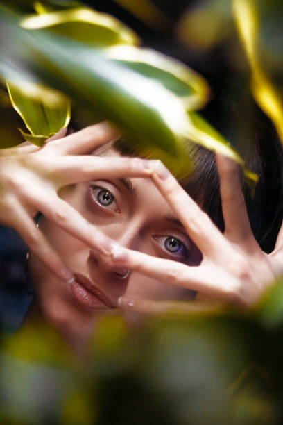 jeune belle femme avec des usines tropicales. beauté naturelle, jeune femme attirante regardant l’appareil-photo tout en restant parmi les feuilles, collage avec le portrait féminin. femme avec le maquillage naturel et les feuilles vertes, belle femme  - beautiful boredom sensuality desire photos et images de collection