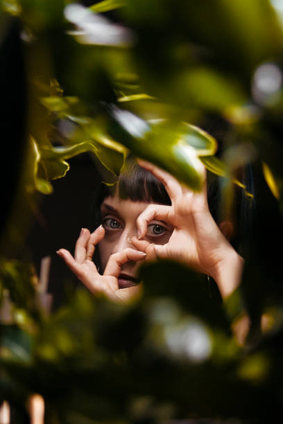 jeune belle femme avec des usines tropicales. beauté naturelle, jeune femme attirante regardant l’appareil-photo tout en restant parmi les feuilles, collage avec le portrait féminin. femme avec le maquillage naturel et les feuilles vertes, belle femme  - beautiful boredom sensuality desire photos et images de collection