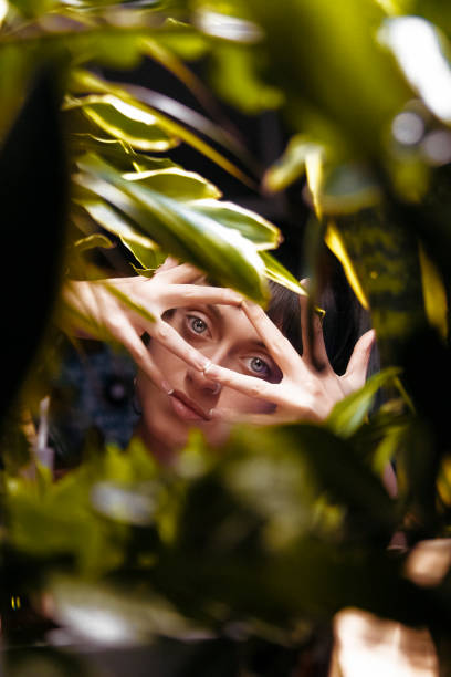 молодая красив�ая женщина с тропическими растениями. природная красота, привлекательная молодая женщина, смотрящ на камеру, стоя среди лист - beautiful boredom sensuality desire стоковые фото и изображения