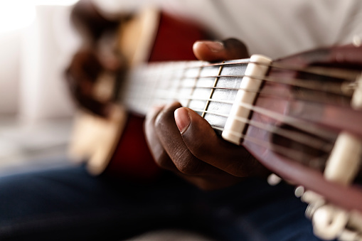 Musician playing on acoustic guitar while sitting on sofa at home during the day,