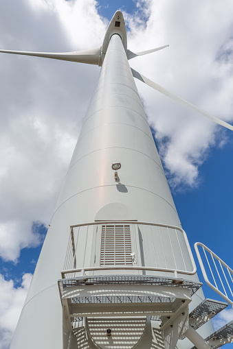 Detailed view of a wind turbine, with central tower pole, technical access stair and entrance door, generator, rotor and blade...