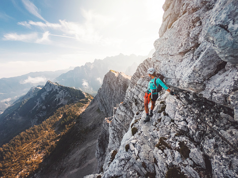 Climber on via ferrata trail, crossing a steep mountain edge