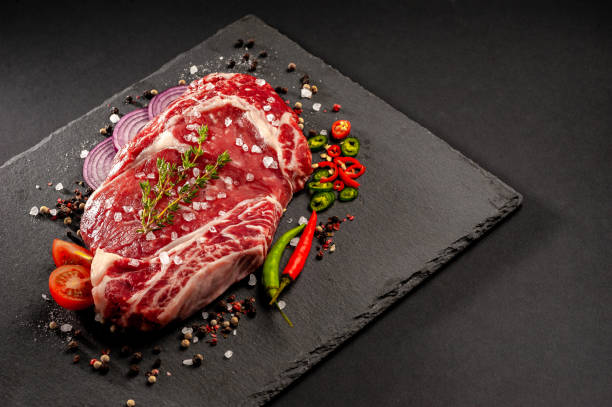 Raw uncooked beef steak. A large piece of meat on the bone lies on a wooden board with spices and fresh herbs. stock photo