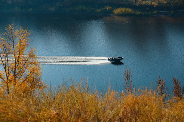 モーターボートは秋の森と丘の間を流れる青い川の真ん中に移動します。美しい景色。 - motorboating jet boat jet boating summer ストックフォトと画像