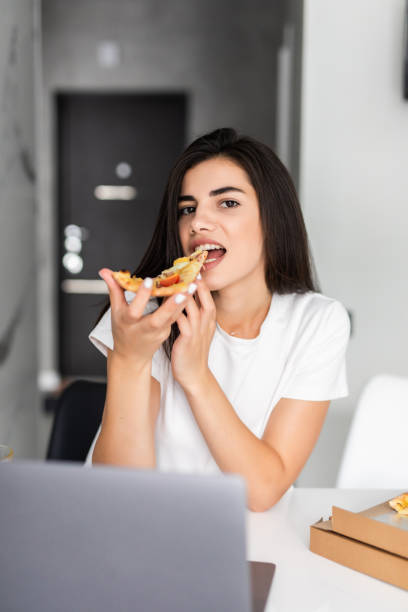 istock Overworked young woman taking a break and eating pizza, working from home on laptop 1284745441