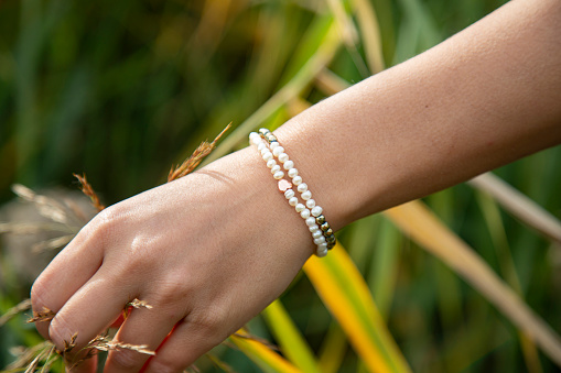 Female hand outdoor touching plants with pearl and hematite bracelet