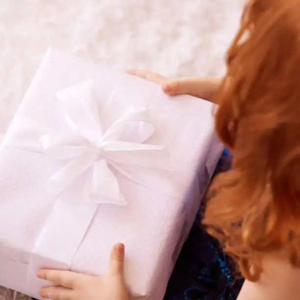 Little girl hold gift box. Red hair child smiling.