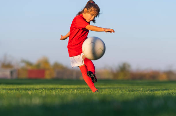 menina chuta uma bola de futebol em um campo de futebol - soccer soccer player kicking soccer ball - fotografias e filmes do acervo