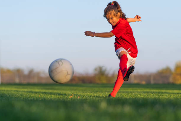 chica patea una pelota de fútbol en un campo de fútbol - patadas fotografías e imágenes de stock