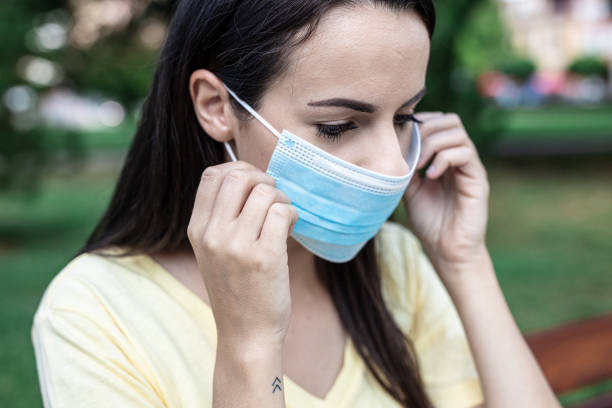istock Young woman putting on face mask in park 1284748972