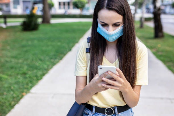istock Woman with protective face mask walking in park and using phone 1284750275