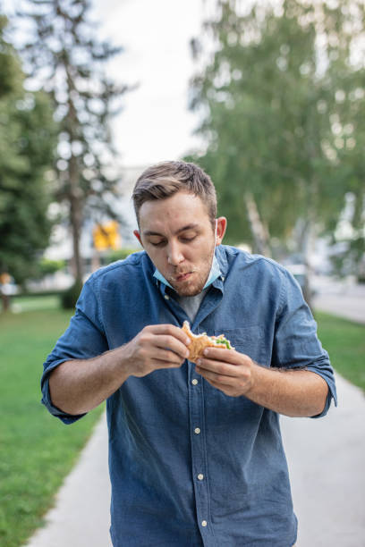 istock Man with face mask under chin walking in park and eating hamburger 1284750319