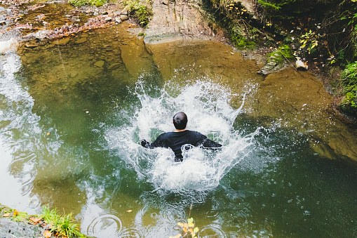 Young man having fun and jumping into the mountain river from the cliff