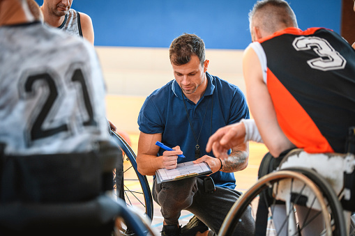 Close-up of coach drawing play diagram for male wheelchair basketball player during practice game.