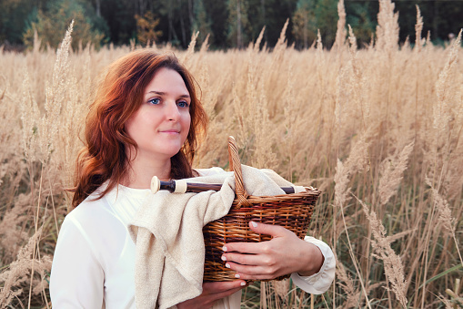 A woman with a basket and a musical instrument flute stands in a field