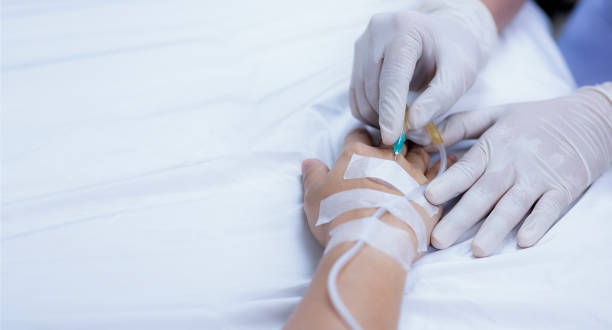 la mano de una enfermera pincha suavemente una aguja médica en la mano de un paciente enfermo para preparar una solución salina y un medicamento para el paciente debilitado - infusion needle fotografías e imágenes de stock