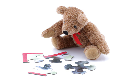 A Teddy bear playing with a jigsaw on white