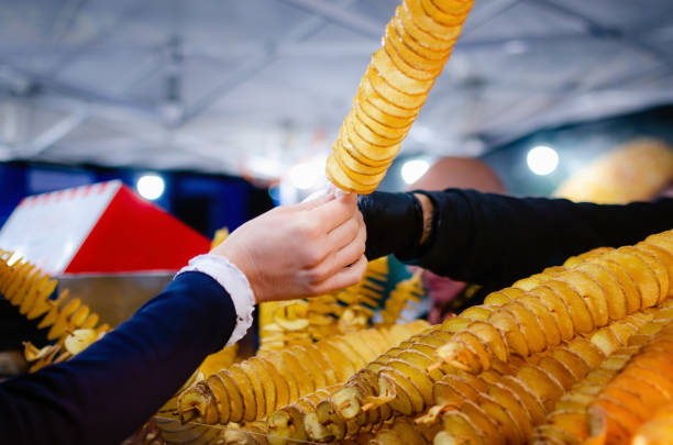 female hand taking a spiral twisted tornado potato from the seller of a street food market stall at evening