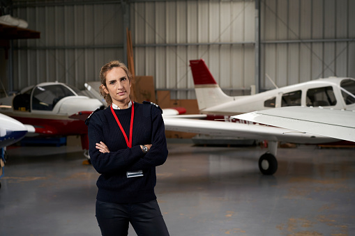 Young pilot posing in the hangar surrounded by airplanes.