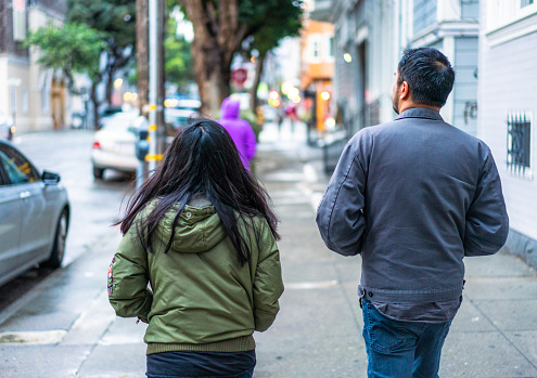A rear view of two friends walking together on the sidewalk in San Francisco's Mission District. Model released image.