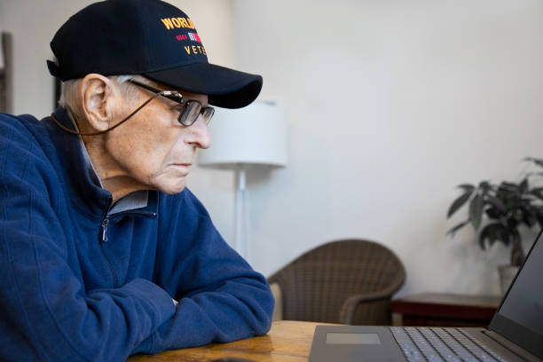istock World War Two Veteran wearing cap at home looking at laptop 1284764007
