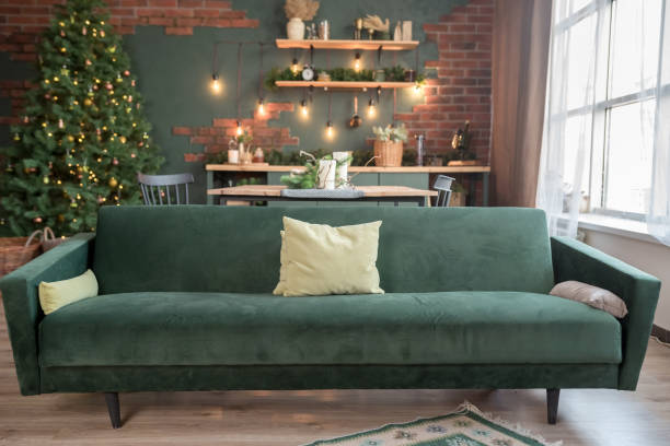 istock Christmas studio interior in white colors during daytime with a chester style sofa, Christmas tree with presents, chest of drawers and two widows at the background 1284768831