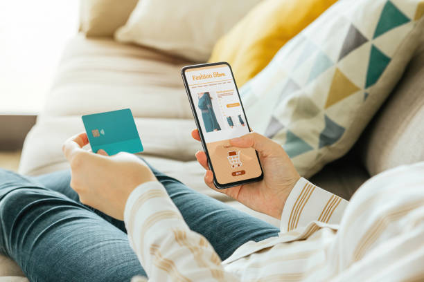 Stock photo of a woman buying a dress online with the phone and a credit card from the sofa at home Stock photo of a woman buying a dress online with the phone and a credit card from the sofa at home. E-commerce concept mobile payment photos stock pictures, royalty-free photos & images