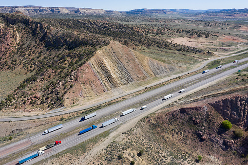 Trucks and cars driving on interstate highway 40 between rock formations, New Mexico, Arizona, USA, aerial view.
