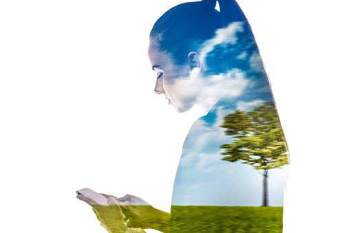 Double exposure of young woman using smartphone and lone tree in meadow