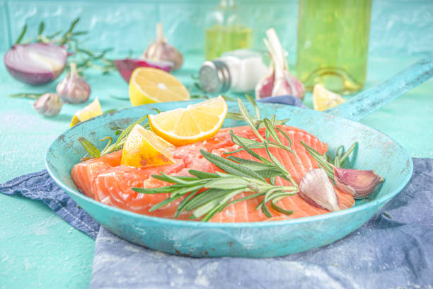 Salmon. Fresh raw salmon fish fillet with cooking ingredients, herbs and lemon in cooking pan, skillet, light blue Turquoise background, top view