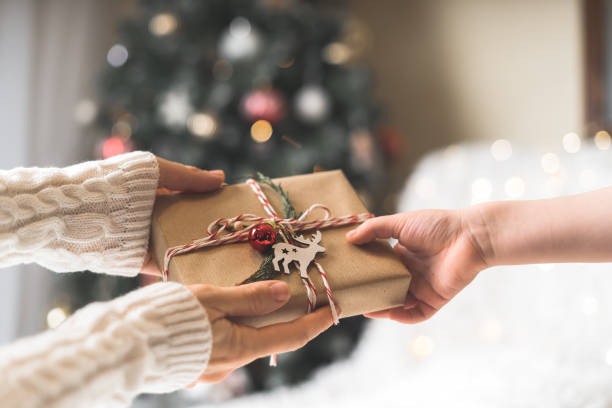 kazak giyen kadın çocuğa sarılmış bir noel hediye kutusu veriyor. parlayan kar bokeh, köknar ağacı. kış tatilleri - yeni yıl hediyesi stok fotoğraflar ve resimler