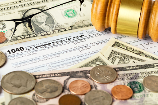 Closeup image of american 1040 Individual Income Tax return form with american dollar money, coins, glasses and judge gavel