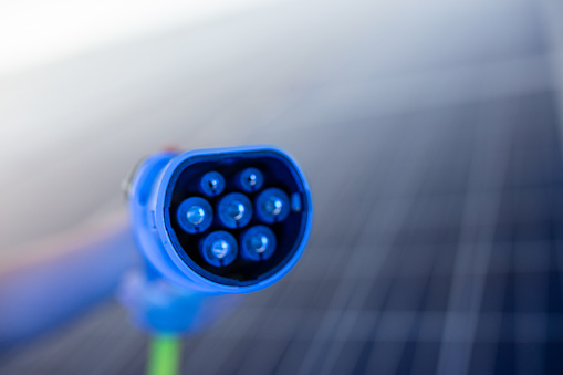 Close-up of a blue electric car charging plug and solar panels in background