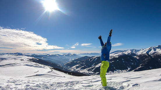 A young man wearing a blue skiing jacket doing yoga at the top of Katschberg, ski resort in Austria. The man spreads open his arms. Yogi's remedy. Solitude and awareness. Winter wonderland