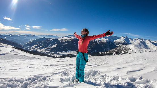 A young woman in colorful skiing outfit doing yoga at the top of Katschberg, ski resort in Austria. The woman spreads open her arms. Yogi's remedy. Solitude and awareness. Winter wonderland