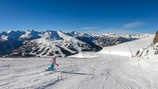 A woman in colorful outfit snowboarding on the slopes of Katschberg in Austria. Panoramic view on the surrounding mountains. Winter wonderland. Sunny winter day. Perfectly groomed slopes
