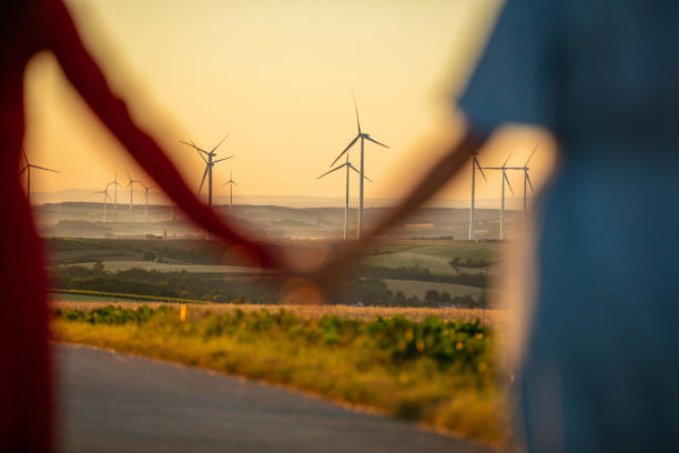 Two people holding hands and looking at rural landscape with wind turbines at dawn
