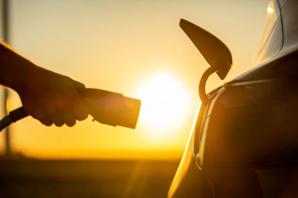 Hand plugging electric charger Close up of hand plugging electric charger to socket in electric car at sunrise motor living stock pictures, royalty-free photos & images