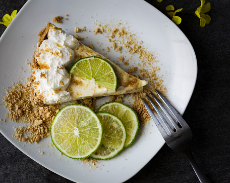 Single slice of key lime pie plated with limes and yellow flowers