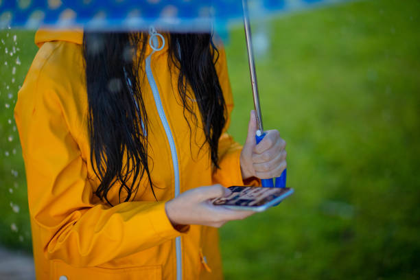 istock Woman in rain jacket and under umbrella using phone in rainy day 1284789496