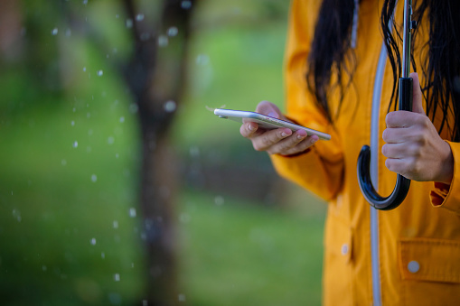 Midsection shot of a woman in a yellow raincoat using her phone