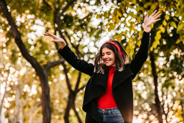 Joyful young beautiful smiling woman listening music and dancing in public park.