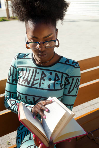 istock Young woman reading at book on street 1284802024