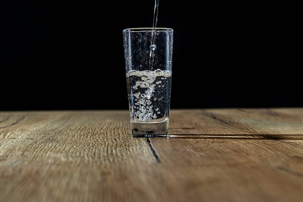 istock pure water is poured into a glass with bubbles on a wooden table with a black background 1284803885