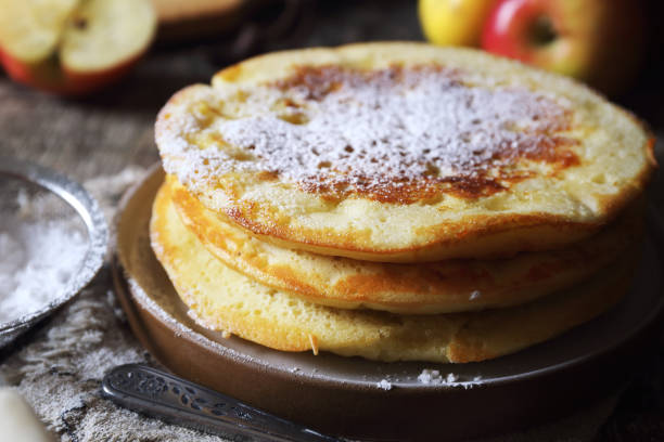Apple pancakes for a breakfast on white plate over light slate, stone or concrete background.